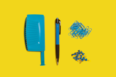 blue plastic modern new office hole puncher, pen and paper clips lying on a yellow background. free...