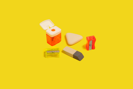 collection of different sharpeners and erasers lying on a yellow background. concept of office...