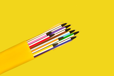 new bright colored pens lying in a box on a yellow background. view from the top. free space for advertising text. concept of office suppliesの写真素材