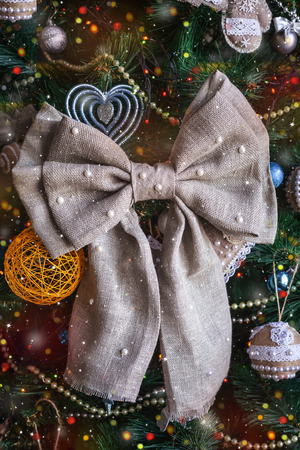 close-up Christmas handmade sackcloth bow on blurred, sparkling tree backdrop. concept of home Happy New Year and Xmas decorの写真素材