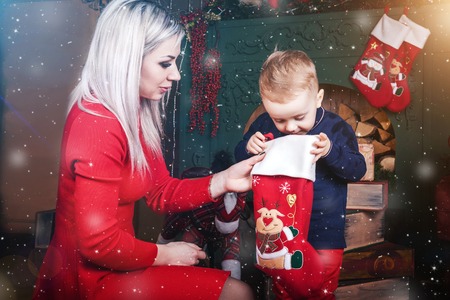 lovely mother and cute baby boy near christmas decorations and ski. mother showing to a child...