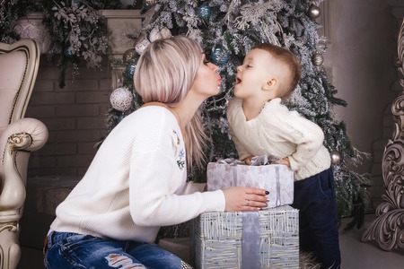 beautiful mother and cute son sitting on the floor near the christmas tree and decorations holding...