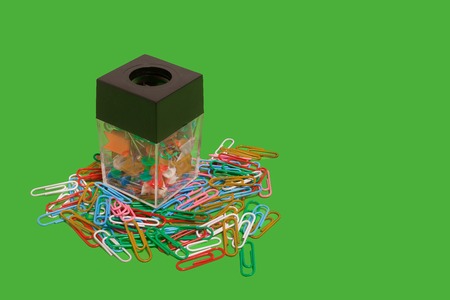different in colours paper clips lying in and out box on a green background. free space for...