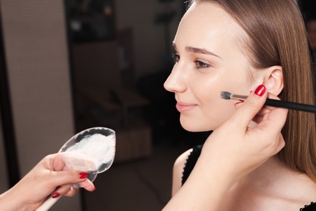 makeup artist dabbing the mixed foundation on a face skin of a young beautiful happy client. concept of professional make up trainingの写真素材