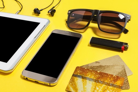 tablet pc, smartphone earphones, cigarette lighter, sunglasses and a gold bank card lying on a...