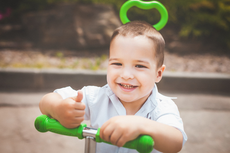 lovely small smiling infant boy riding a green trike in the park. concept of happy childhoodの写真素材