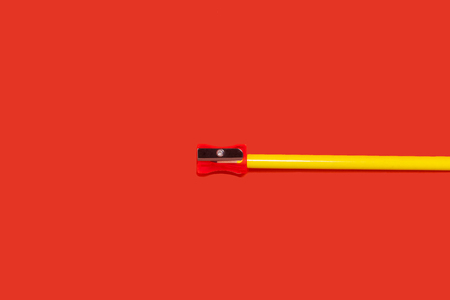new yellow pencil lying with a small sharpener on its top on a red background. concept of office and school suppliesの写真素材
