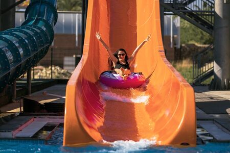 happy woman coming down on the rubber ring by the orange slide in the aqua park. Summer Vacation. Weekend on resortの写真素材