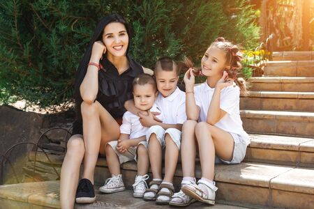 beautiful mother with her three happy joyful cute children sitting on stairs in the park. concept of love and familyの写真素材