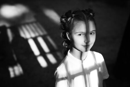 cute little thoughtful girl standing at the night playground. shadows from gungle gym falling on her face and body. black and white photoの写真素材