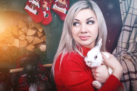 beautiful blonde smiling woman hugging a cute rabbit sitting on the floor. On the background Christmas decorationsの写真素材