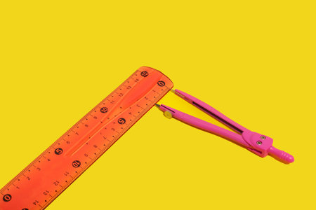 Pair of pink metal dividers lying near an orange ruler on a yellow background. free space for text....