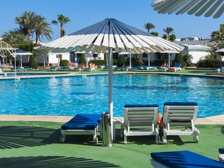 Large white pool umbrella and two sun loungers for a good stay. Rest in a tropical countryの写真素材