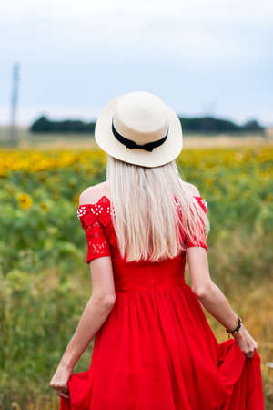 Unrecognizable beautiful girl running through yellow sunflower field. Young woman in red dress showing joyful emotions jogging through meadow at summer day. Happiness and freedom conceptの写真素材