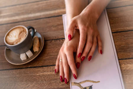 Women's hands hold the menu in the restaurant. A cup of coffee on the table and a clean menu. A girl in a restaurant, a photo of her hands. Hands on the table. Breakfast in the cafeの写真素材