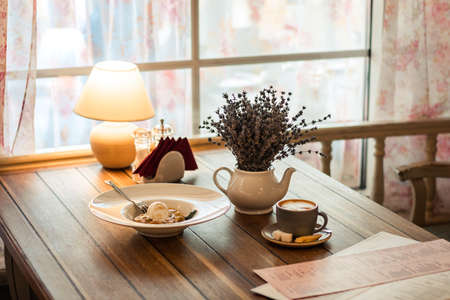 Table with food in the restaurant. A cup of coffee, food, a yellow lamp and a bouquet of flowers. A table is laid out by the window. Breakfast in the restaurant. Cafeteriaの写真素材