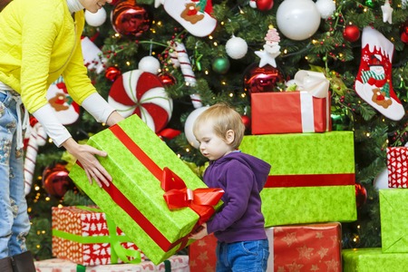Mom gives a gift to the kid on the background of the Christmas treeの写真素材