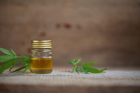 A cannabis leaf and a bottle of hemp oil on a wooden tableの写真素材