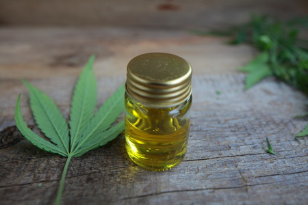 A cannabis leaf and a bottle of hemp oil on a wooden tableの写真素材