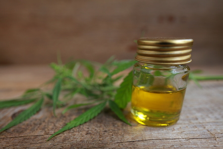 A cannabis leaf and a bottle of hemp oil on a wooden tableの写真素材
