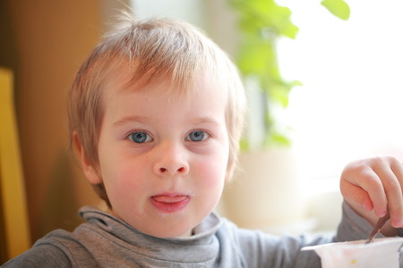 the child eats yogurt with a spoon sitting at the table