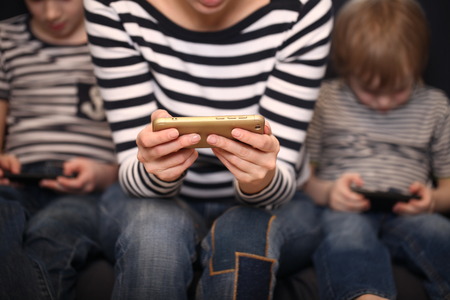 mother with two brothers blond boys on a blue sofa at home playing smartphonesの写真素材