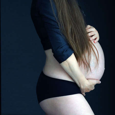 pregnant woman holding her belly on a dark background with her handsの写真素材
