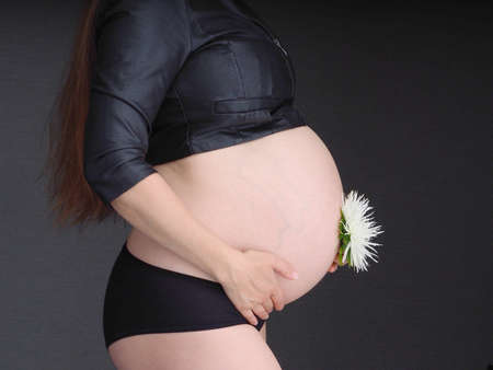 pregnant woman holding her belly on a dark background with her hands