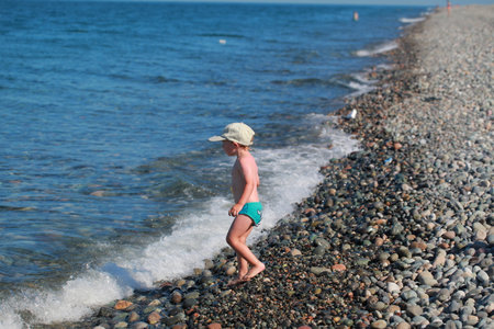 kid shoots from a water gun on the seashore. Pebble beachの写真素材