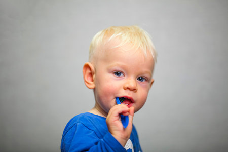 blond baby in a blue T-shirt brushes his teeth with a blue brushの写真素材