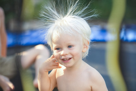 Cute little boy with static electricy hair, having his funny portrait taken outdoors on a trampolineの写真素材