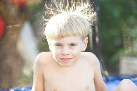 Cute little boy with static electricy hair, having his funny portrait taken outdoors on a trampolineの写真素材