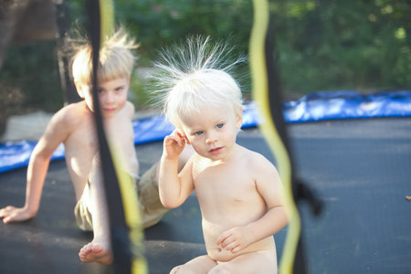Cute little boy with static electricy hair, having his funny portrait taken outdoors on a trampolineの写真素材