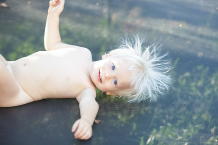 Cute little boy with static electricy hair, having his funny portrait taken outdoors on a trampolineの写真素材