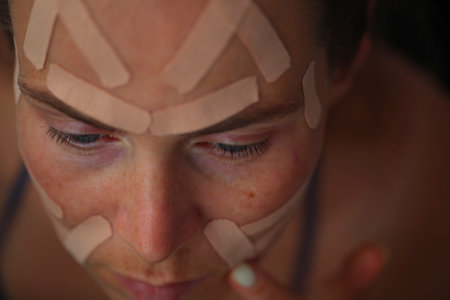 Portrait pretty young woman with kinesio taping on her face in front of a mirror. Home facial skin...