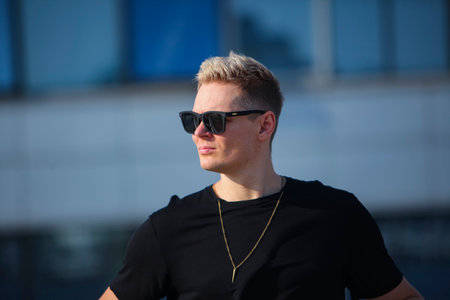 Handsome young man with short blond hair wearing black t-shirt and sunglasses in an urban contextの写真素材