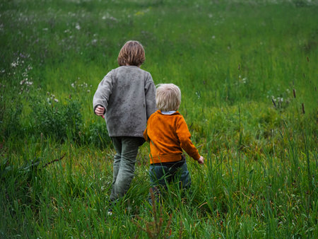 Two little boys walking in the green meadow. Back view.の写真素材