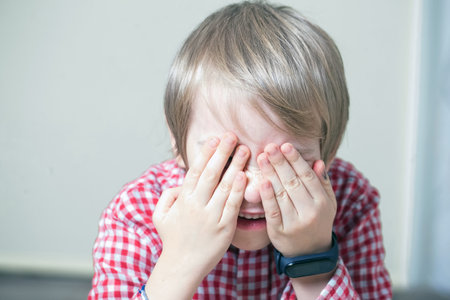 Little boy in a checkered shirt closing his eyes with his hands