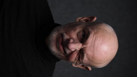 Portrait of a bald man in a black T-shirt on a dark backgroundの写真素材