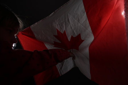 Little girl holding a Canadian flag in front of her face on dark background