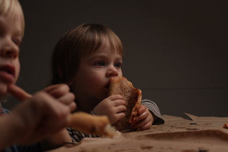 children two boys eating pizza at home sitting at the tableの写真素材