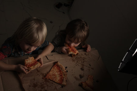 children two boys eating pizza at home sitting at the tableの写真素材