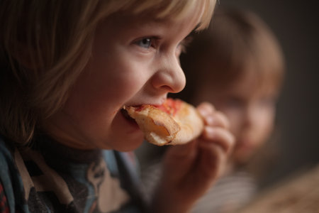 children two boys eating pizza at home sitting at the tableの写真素材