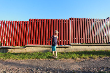 blond boy in blue t-shirt and shorts against wall summerの写真素材