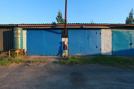blond boy in blue t-shirt and shorts against wall summerの写真素材