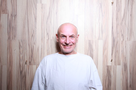 Portrait of a smiling bald man in a white T-shirt on a wooden backgroundの写真素材