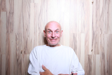 Portrait of a bald man in a white T-shirt on a wooden background
