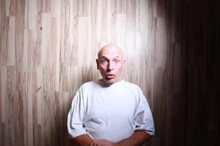 Portrait of a bald man in a white T-shirt on a wooden backgroundの写真素材