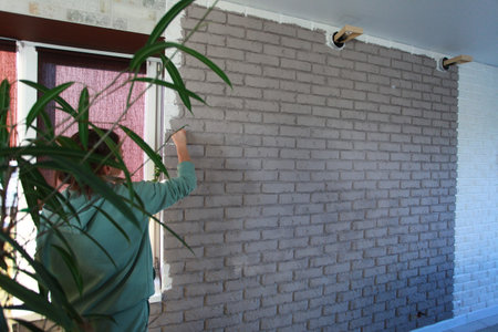 Worker painting white brick wall with paint roller, closeup of photoの写真素材