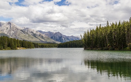 Forest reflect on the surface of Johnson Lake cloudy day - Banff National Park, Alberta, Canadaの写真素材